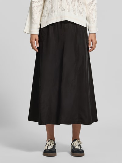 Frauenmodel trägt Midirock mit Eingrifftaschen von Marc Cain in Schwarz, A-Linie, Teilungsnähte, glatte Textur, Nahaufnahme Oberkörper.