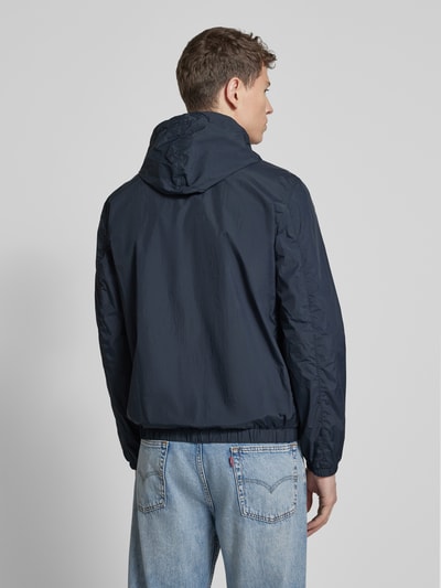 Męski model nosi Kurtkę z kapturem model 'NIGLE' od Peuterey, krój regular fit, zamek błyskawiczny dwustronny, wpuszczane kieszenie, długość tyłu w rozmiarze M 69 cm, szerokość ramion w rozmiarze M 47 cm, szerokość klatki piersiowej w rozmiarze M 56 cm, długość rękawów w rozmiarze M 68 cm, kolor granatowy, pełny widok z tyłu.