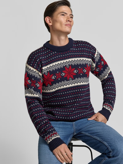 Männermodel trägt Regular Fit Wollpullover in Strick-Optik Modell 'Egersund' von Dale of Norway in Blau, Rot, Weiß, Ganzkörperansicht von vorne. Herren Wollpullover aus reiner Wolle, Rückenlänge 64 cm, Ärmellänge 58 cm.