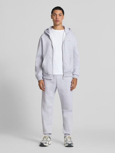 Męskymodel prezentuje Slim Fit Sweatpants mit Tunnelzug od REVIEW w jasnoszarym kolorze, wpuszczane kieszenie, kieszeń z tyłu, elastyczny pas z tunelem, krój slim fit, długość wewnętrzna nogawki w rozmiarze M: 80 cm, widok całej sylwetki z przodu.