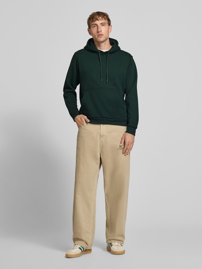 Männermodel trägt Hoodie mit Känguru-Tasche Modell 'BRADLEY' von JACK & JONES, dunkelgrün, lockerer Schnitt, Ganzkörperansicht von vorne.