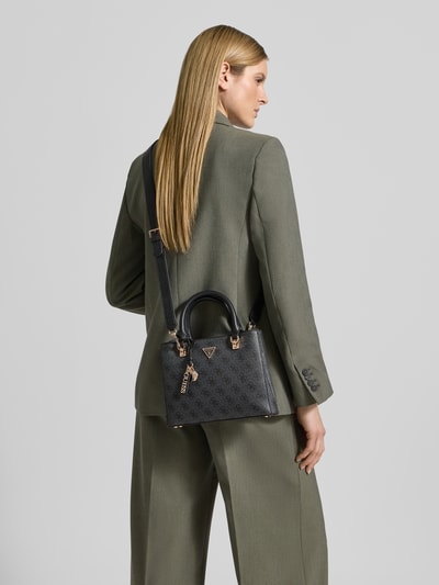Frauenmodel trägt Handtasche mit Logo-Muster Modell 'NOELLE II' von Guess, schwarze Textur, Label-Applikation, Schulterriemen, Ganzkörperansicht Rückansicht. Breite 24 cm, Länge 19 cm, Tiefe 6 cm, Länge Schulterriemen 126 cm, Hauptfach mit Reißverschluss.