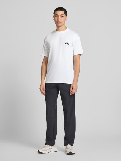 Männermodel trägt T-Shirt mit Rundhalsausschnitt und Logo von Quiksilver, Material-Mix mit Stretch-Anteil, Regular-Fit, Herren T-Shirt, Rückenlänge bei Größe M: 75 cm, weiße Farbe, glatte Struktur, Ganzkörperansicht von vorne.