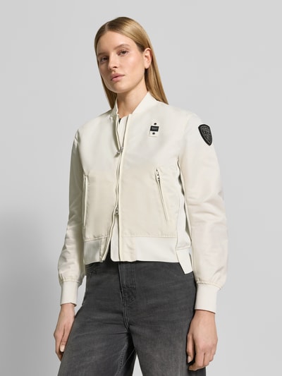 Frauenmodel trägt Bomberjacke mit Reißverschlusstaschen Modell 'LAURIE' von Blauer Usa in Creme mit Label-Patches, Nahaufnahme Oberkörper. Lose Passform mit gerippten Abschlüssen, Stehkragen und Zweiwege-Reißverschluss.