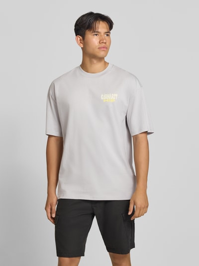 Männermodel trägt Relaxed Fit T-Shirt aus reiner Baumwolle Modell 'Luggage' von Carhartt Work In Progress, hellgrau, Ganzkörperansicht von vorne