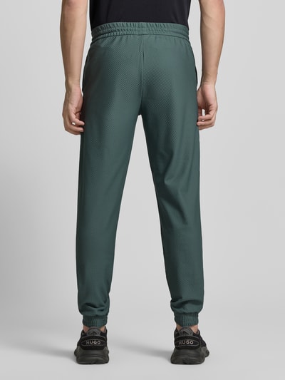Männermodel trägt Regular Fit Sweatpants mit Strukturmuster von EA7 Emporio Armani, Elastischer-Material-Mix, Eingrifftaschen, elastischer Bund mit Tunnelzug, Farbe dunkles Grün, Ganzkörperansicht Rückansicht.