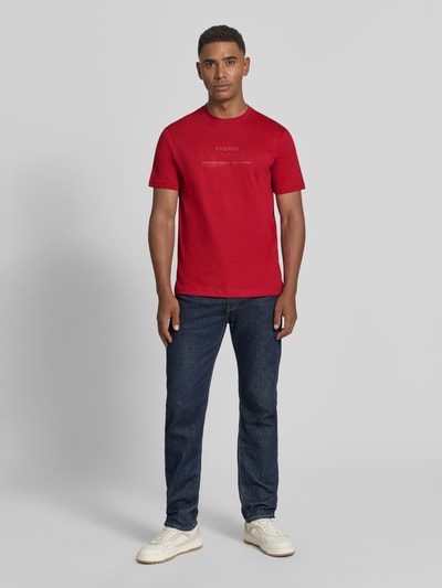 Männermodel trägt Slim Fit T-Shirt aus reiner Baumwolle mit Logo-Print von Armani Exchange in Rot, kurzärmelig, Ganzkörperansicht von vorne.