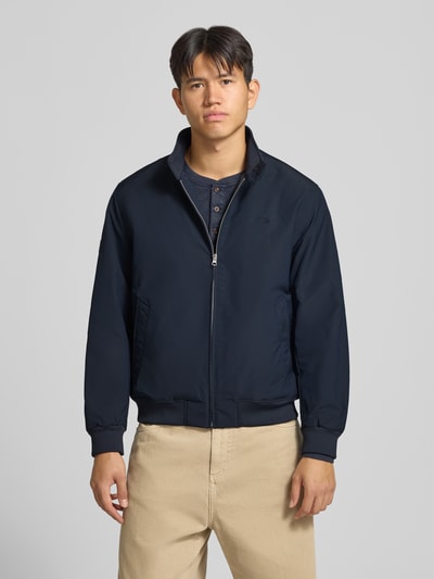 Männermodel trägt Regular Fit Jacke mit Logo-Stitching Modell 'HARRINGTON' von Superdry in Dunkelblau, Ganzkörperansicht von vorne. Elastischer Material-Mix, Stehkragen, Reißverschluss. Rückenlänge 66 cm, Schulterbreite 50 cm, Brustweite 60 cm, Ärmellänge 65 cm.