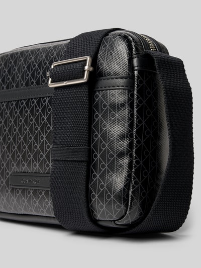 Produktfoto, Handtasche mit Logo-Muster und Schulterriemen von CK Calvin Klein, Herren, Hauptfach mit Reißverschluss, Label-Detail, verstellbarer Schulterriemen, Maße 22x16x5 cm, Schulterriemenlänge 106 cm, schwarze Textur mit silbergrauen Mustern.