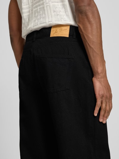 Mężczyzna nosi Loose Fit Jeans im 5-Pocket-Design Modell 'Roi' od Les Deux, czarna bawełna, skórzana naszywka, detal z tyłu, zdjęcie z tyłu. Szerokość w rozmiarze 32/32: 40 cm, długość wewnętrzna nogawki: 78 cm.