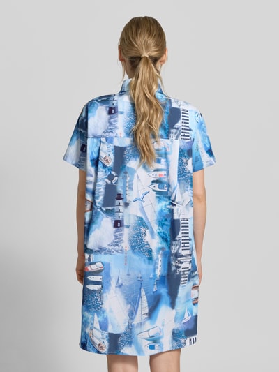 Vrouwenmodel draagt Relaxed Fit Hemdblusenkleid met all-over fotoprint van Marc Cain in blauw- en wittinten, puur katoen, platte kraag, knoopsluiting, korte mouw, ruglengte maat 36: 94 cm, borstwijdte maat 36: 56 cm, mouwlengte maat 36: 18 cm. Ganzkörperansicht Rückansicht.