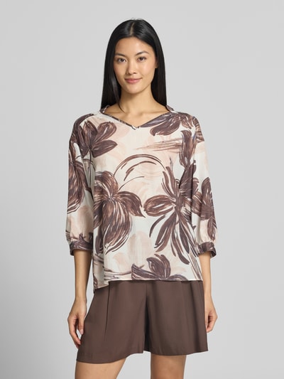 Frauenmodel trägt Relaxed Fit Bluse aus Viskose-Mix mit floralem Allover-Print von MORE & MORE, helle und braune Töne, V-Ausschnitt, 3/4-Arm, Ganzkörperansicht von vorne.