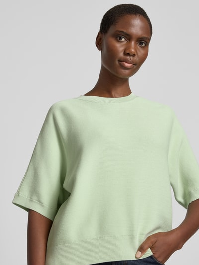 Kobiece modelka nosi sweter z dzianiny z mieszanki wiskozy, krój regular fit, model 'Thamira' od MSCH Copenhagen, rękaw o dł. 1/2, okrągły dekolt, długość tyłu 54 cm w rozmiarze S/M, długość rękawów 34 cm, miękka faktura, pastelowy zielony, zbliżenie na górną część ciała.