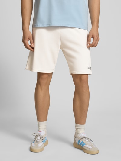 Männermodel trägt Regular Fit Shorts mit Label-Stitching von REVIEW in Creme aus Baumwoll-Mix, elastischer Bund, Nahaufnahme Beine, Ganzkörperansicht von vorne. Bundweite 44 cm, Innenbeinlänge 22 cm, Regular-Fit Herren Shorts.