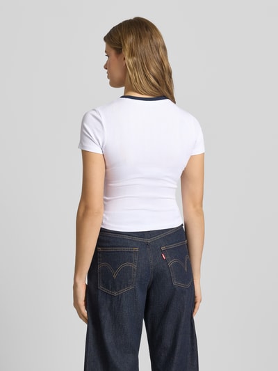 Frauenmodel trägt T-Shirt mit Rundhalsausschnitt und Label-Stitching von Guess Jeans aus Baumwoll-Mix mit Modal-Anteil, Cropped, Rückenlänge 45 cm, Ganzkörperansicht Rückansicht.