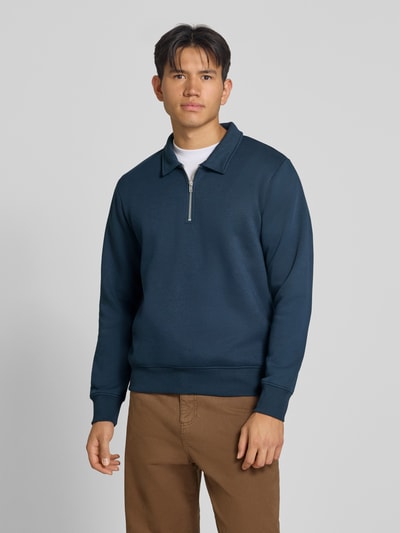 Męski model nosi Regular Fit Sweatshirt mit Baumwoll-Anteil Modell 'Bradley' von JACK & JONES, Mieszanka materiałów, krój regular fit, kołnierz zapinany, zamek błyskawiczny, Długość tyłu w rozmiarze M: 69 cm, granatowa góra, brązowe spodnie, gładka tekstura, całkowity widok z przodu.