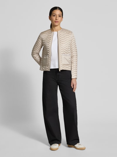 Frauenmodel trägt beigefarbene Slim Fit Steppjacke mit aufgesetzten Taschen Modell 'Tamina' von SAVE THE DUCK, Ganzkörperansicht von vorne.