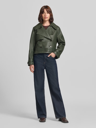 Modelka kobieca nosi kurtka skórzana Regular Fit Lederjacke aus echtem Lammleder model 'Satela1' von BOSS w kolorze ciemnej zieleni na tle neutralnym, widok całej sylwetki z przodu, kurtka z gładką teksturą, kontekst: damska kurtka skórzana od BOSS.