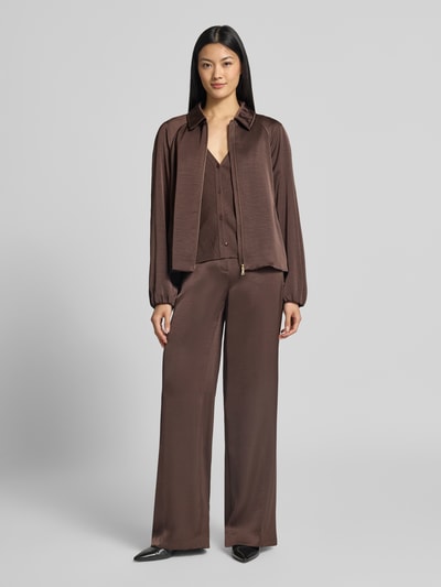 Frauenmodel trägt schimmernde Wide Fit Hose mit Bindegürtel von Marc Cain, High Waist, brauner Glanzstoff, fließende Struktur, Ganzkörperansicht von vorne.