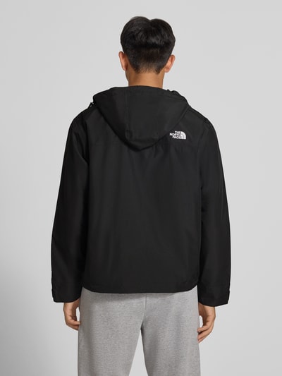 Męski model ma na sobie czarną kurtkę z kapturem Jacke mit Label-Stitching Modell 'REIGN ON 2.0' von The North Face, krój regular fit, gładka tekstura, widoczne szwy z tyłu, długość tyłu w rozmiarze M: 69 cm, szerokość ramion w rozmiarze M: 52 cm, szerokość klatki piersiowej w rozmiarze M: 63 cm, długość rękawa w rozmiarze M: 65 cm, widok całej sylwetki z tyłu.