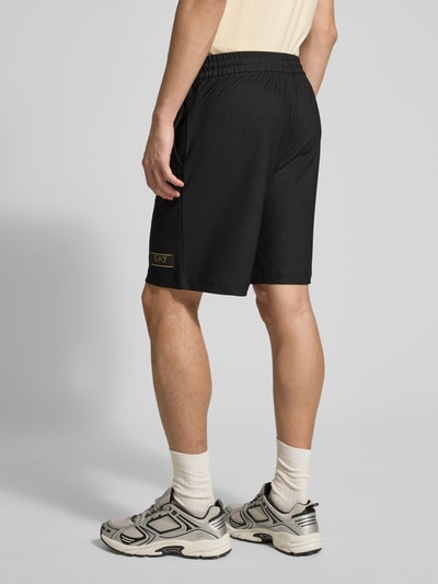 Männermodel trägt Regular Fit Shorts mit Strukturmuster von EA7 Emporio Armani in Schwarz mit elastischem Bund, Ganzkörperansicht Rückansicht.