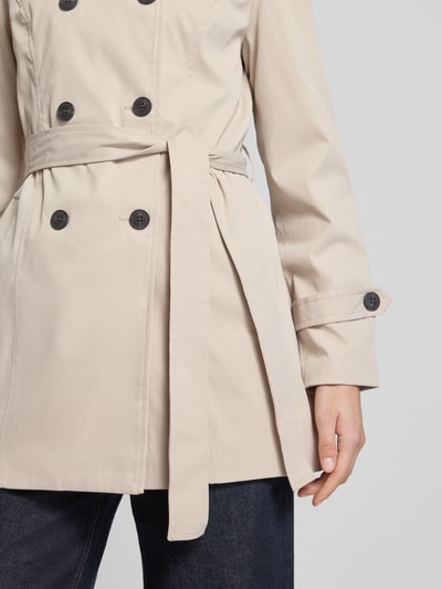 Kobiece modelka nosi Regular Fit Trenchcoat mit Taillengürtel zum Binden Modell 'CHALSEA OLIVIA' von Vero Moda, efekt: jednolity kolor, krój regular fit, wykładany kołnierz, listwa guzikowa 2-rzędowa, szwy, długi rękaw z patką, wpuszczane kieszenie, wykończenie materiału: splot twill; zbliżenie na górną część ciała.