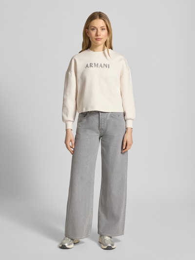 Frauenmodel trägt Sweatshirt mit Logo-Print und Rundhalsausschnitt von ARMANI EXCHANGE in Beige, Baumwoll-Mix mit Stretch-Anteil, Loose Fit, Ganzkörperansicht von vorne.