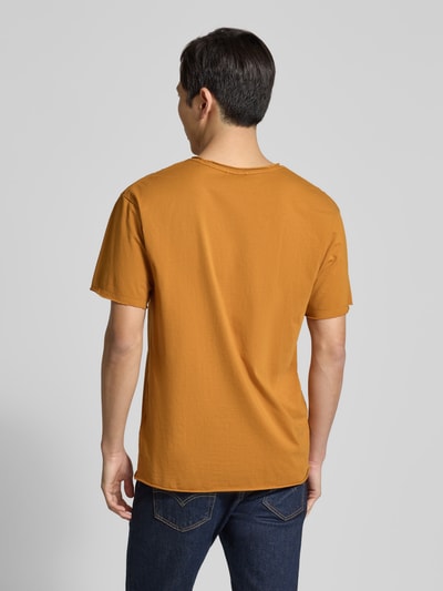 Männermodel trägt T-Shirt mit Rundhalsausschnitt und Label-Detail von Scotch & Soda in Ocker, Reine Baumwolle, Regular-Fit, Rollsaum, Ganzkörperansicht Rückansicht. Rückenlänge bei Größe M: 67 cm.