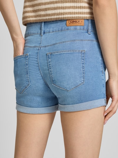 Frauenmodel trägt Regular Fit Jeansshorts aus Baumwoll-Mix Modell 'CARMEN' von Only in Denim-Optik mit Label-Patch, 5-Pocket-Design, fixiertem Umschlag, Knopf und verdecktem Reißverschluss, Ganzkörperansicht Rückansicht.