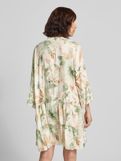 Frauenmodel trägt Minikleid aus Viskose mit Serafino-Kragen Modell 'Ge44rdaa' von ZABAIONE mit floralem Muster, Ganzkörperansicht Rückansicht. Loose Fit, zarte Grün- und Beigetöne, weiche Textur, Rückenlänge 89 cm, Brustweite 62 cm, Ärmellänge 47 cm.