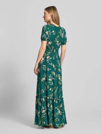 Modelka nosi Maxikleid aus Viskose mit V-Ausschnitt od marki Apricot, zielony wzór allover, elastyczny pas, długość 123 cm, szerokość w rozmiarze S 32 cm, długość rękawa 22 cm, całkowity widok z tyłu.