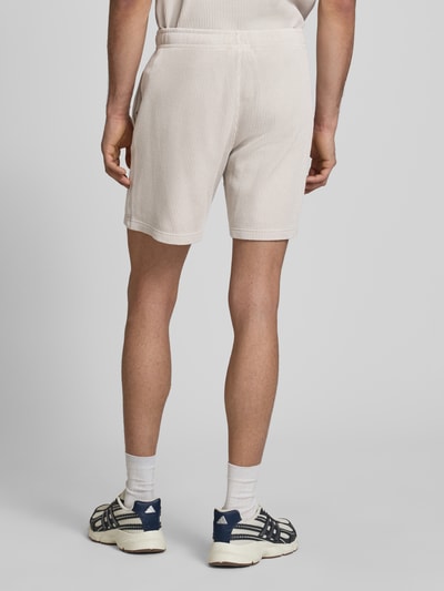 Mężczyzna nosi Shorts mit Strukturmuster und elastischem Bund od CHAMPION, bawełniany miks, krój regular fit, jasny kolor, strukturalny wzór, elastyczny pas z label-stitching, szerokość w rozmiarze M: 40 cm, długość nogawki od wewnątrz: 19 cm, widok całej sylwetki od tyłu.