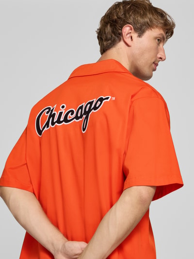 Männermodel trägt Relaxed Fit Freizeithemd aus Baumwoll-Mix von Champion in kräftigem Orange mit Statement-Stitching und Reverskragen, Rückenansicht, Kontext: kurzärmeliges Design, elastischer Baumwoll-Mix, Rückenlänge 74 cm, Schulterbreite 41 cm, Ärmellänge 36 cm
