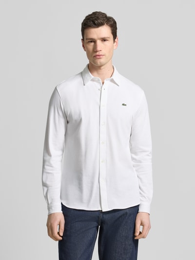 Männermodel trägt Slim Fit Freizeithemd aus reiner Baumwolle von Lacoste in Weiß, Optik: Unifarben, Logo-Stitching, Ganzkörperansicht von vorne.