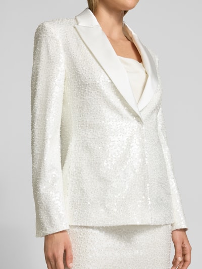 Frauenmodel trägt Blazer mit Paillettenbesatz und Reverskragen von Marc Cain, taillierter Schnitt, cremeweiß, strukturierte Oberfläche, Nahaufnahme Oberkörper.
