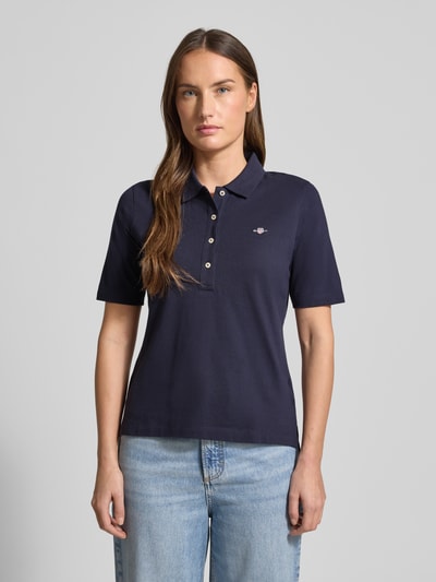 Frauenmodel trägt Poloshirt aus Baumwolle mit Label-Detail von GANT, gerade geschnitten, Polokragen, kurze Knopfleiste, 1/2-Arm, Farbe Dunkelblau, feine Struktur, Rückenlänge bei Größe S 59 cm, Nahaufnahme Oberkörper