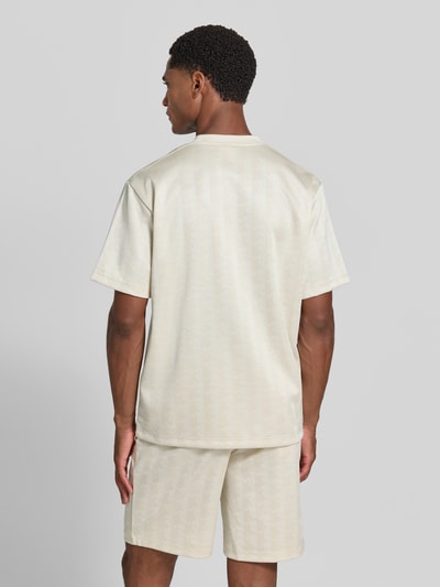 Männermodel trägt Regular Fit T-Shirt mit Allover-Muster von Lacoste in hellem Beige, lockere Passform, Ganzkörperansicht Rückansicht. Herren T-Shirt von Lacoste.