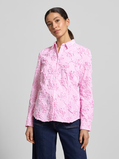 Modelka kobieca nosi HBK Zümdholzstreifen Streifen Bluse mit Blumen Applikationen von Christian Berg Woman, różowe i białe paski, bawełniany materiał, luźny krój, aplikacje kwiatowe, kołnierzyk koszulowy, zapięcie na guziki, długość tyłu 62 cm, długość rękawa 60 cm, widok całej sylwetki od przodu.