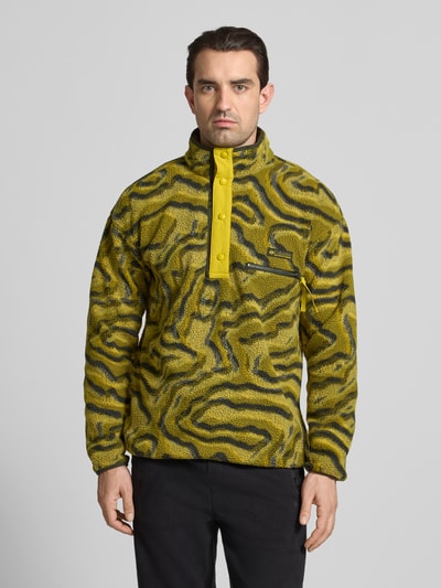 Männermodel trägt Regular Fit Pullover mit Logo-Patch von Columbia in gelber Fließ-Optik mit Brusttasche, Druckknopfleiste, Ganzkörperansicht von vorne.