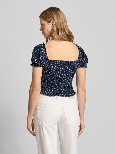 Frauenmodel trägt Slim Fit Blusentop mit Allover-Muster Modell 'HILLARY' von Only in Dunkelblau mit floralem Muster, Cropped-Länge, ohne Kragen, Henley-Ausschnitt, Kurzarm mit Raffungen, Optik: Allover-Muster, Ganzkörperansicht Rückansicht.