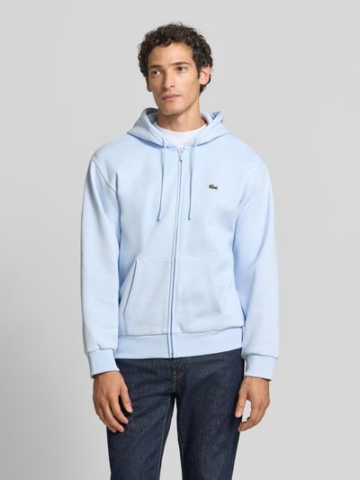 Männermodel trägt Regular Fit Sweatjacke aus Baumwoll-Mix von Lacoste in Hellblau, glatte Struktur, Reißverschluss, Vorderansicht, Nahaufnahme Oberkörper.