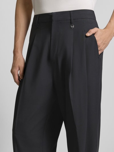 Mężczyzna nosi Stoffhose mit Label-Detail von Antony Morato, czarny materiał z domieszką wiskozy, luźny krój, szeroki elastyczny pas, francuskie kieszenie, kieszenie tylne, miękka faktura, szerokość w rozmiarze 50: 44 cm, długość nogawki wewnętrznej: 78 cm, zbliżenie na biodra i talię.