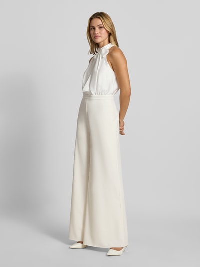 Frauenmodel trägt Jumpsuit mit Stehkragen von SWING, cremefarben, taillierte Passform, ärmellos, Zierschleife, Ganzkörperansicht von vorne.