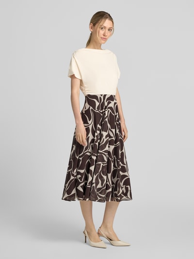Frauenmodel trägt Cocktailkleid im 2-in-1-Look mit Drapierungen von Christian Berg Cocktail, A-Linie, Midikleid, abstraktes Muster, cremefarbene Oberpartie, braun-beiger Rock, Rückenlänge bei Größe 36: 116 cm, Brustweite bei Größe 36: 45 cm, Ganzkörperansicht von vorne.
