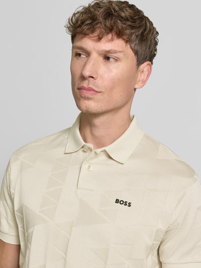 Męskimodel nosi koszulkę polo Regular Fit Poloshirt model 'PL_NETWORK JQ PIRAX' od BOSS Green w jasnym beżu z geometrycznym wzorem, zbliżenie na górną część ciała.
