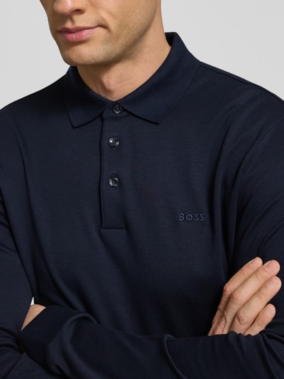 Männermodel trägt Poloshirt mit Label-Schriftzug von BOSS in Dunkelblau, Reine Baumwolle, Gerader-Schnitt, Polokragen, Modell 'Pado 30', Langärmlig, Knopfleiste, Gerippte Ärmelabschlüsse, Nahaufnahme Oberkörper.