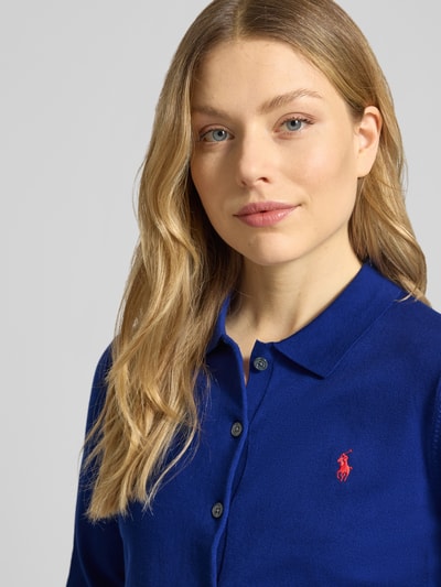 Vrouwenmodel draagt Slim Fit gebreid jack uit katoenmix van Polo Ralph Lauren, look: effen kleuren, fijngebreid, logostitching, overhemdkraag, lange mouw, knoopsluiting, geribde rompzoom en mouwboorden, detailopname bovenlichaam.