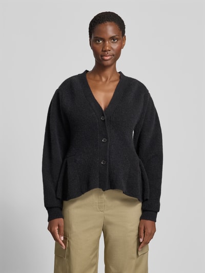 Frauenmodel trägt schwarzen Relaxed Fit Cardigan aus Alpaka-Mix von ROTATE mit Strick-Optik, Volant-Saum und Knopfleiste, Ganzkörperansicht von vorne, Rückenlänge 56 cm bei Größe S, elastischer Woll-Anteil.