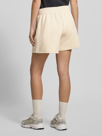 Frauenmodel trägt Shorts mit elastischem Bund von adidas Sportswear in Beige, lockerer Schnitt, Baumwoll-Mix, Label-Print, Ganzkörperansicht Rückansicht.