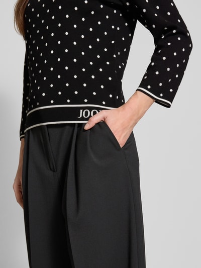 Frauenmodel trägt schwarzen Strickpullover aus Viskose-Mix Modell 'Konstantina' von JOOP! mit weißen Punkten, Nahaufnahme Oberkörper.